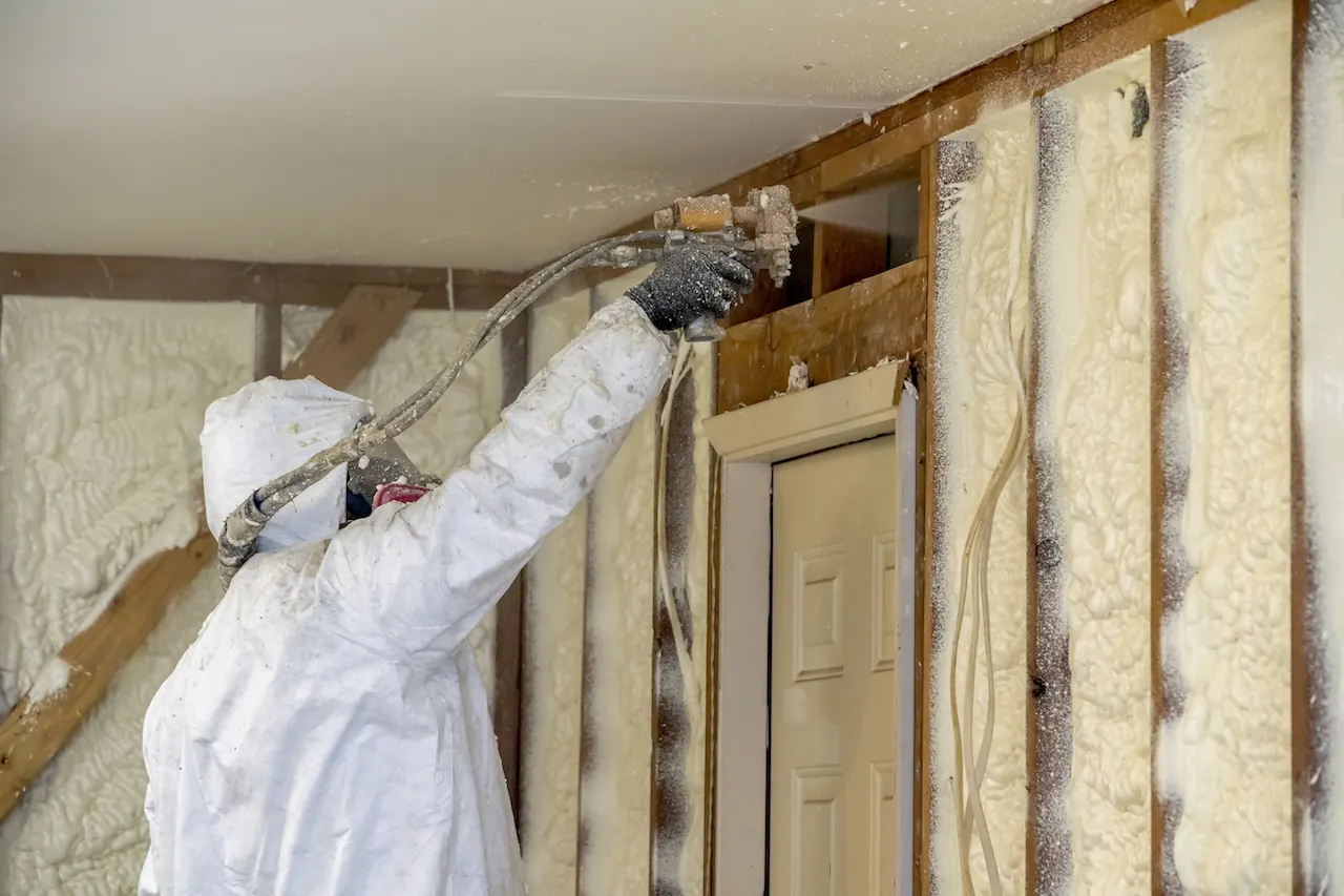 Installer spraying foam insulation into an open wall cavity beside a doorway inside a house
