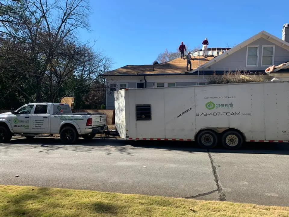 Crew working on a house roof beside the Green Earth truck and trailer parked at the kerb.