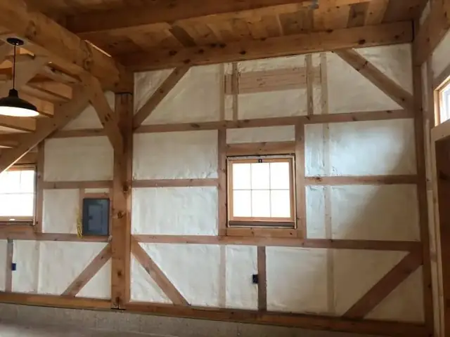 Timber-framed room with spray foam applied between heavy posts and beams around a window.