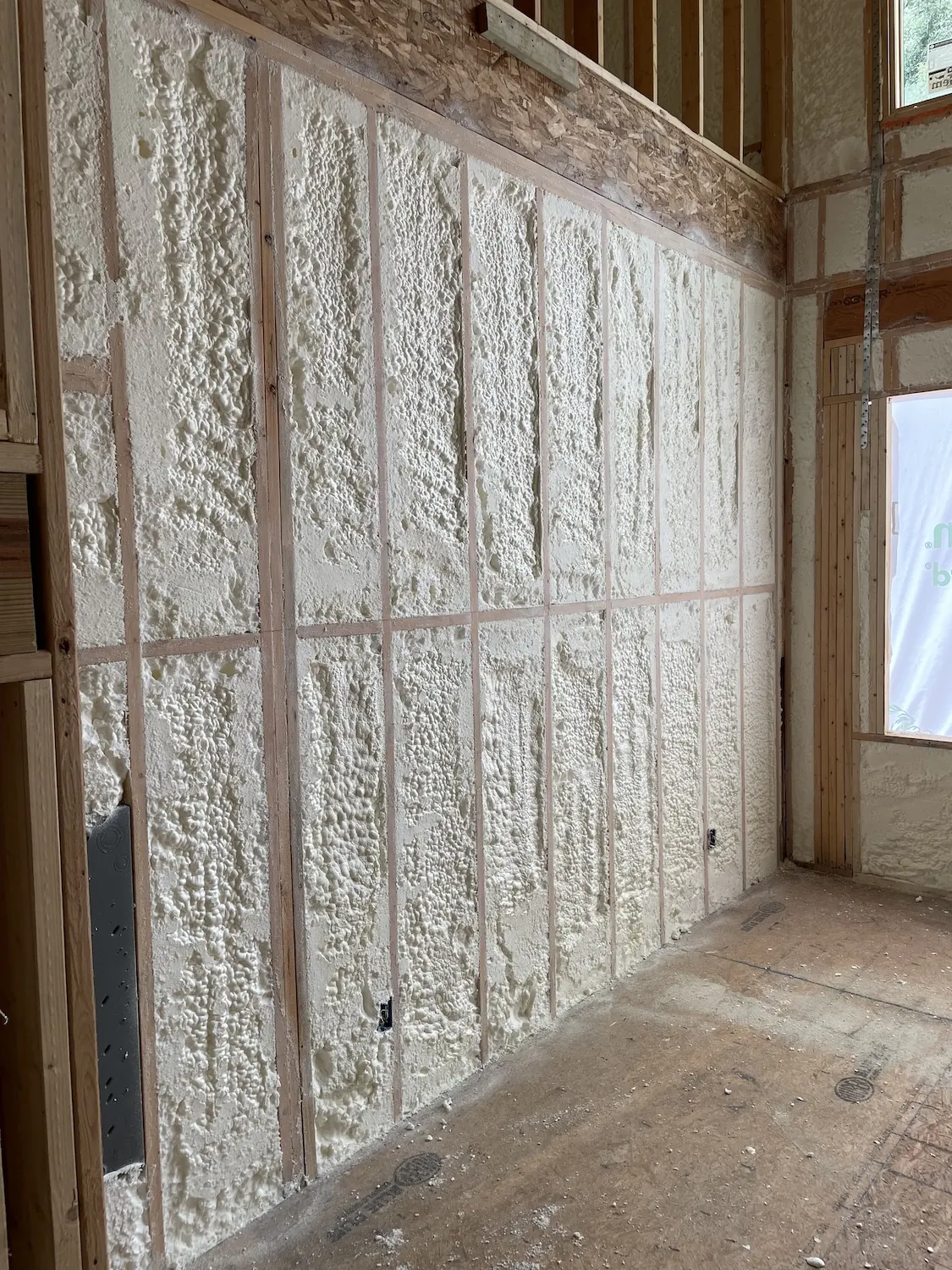Timber stud wall filled flush with white spray foam in a building under construction.