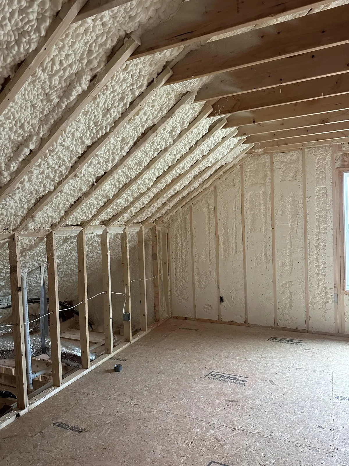 Unfinished attic room with spray foam applied across the sloped ceiling and the end wall framing