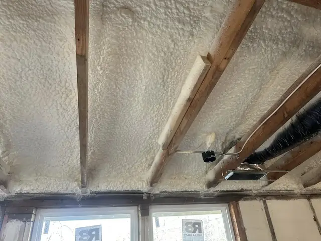 Ceiling and rafters coated in spray foam above newly installed windows in a room being renovated.