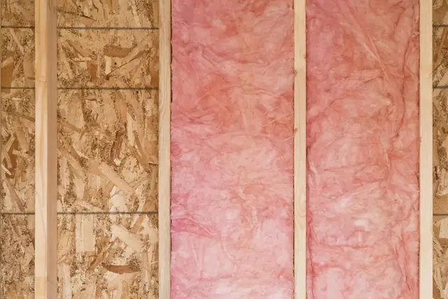 Pink fiberglass batt insulation installed between wall studs next to exposed sheathing.