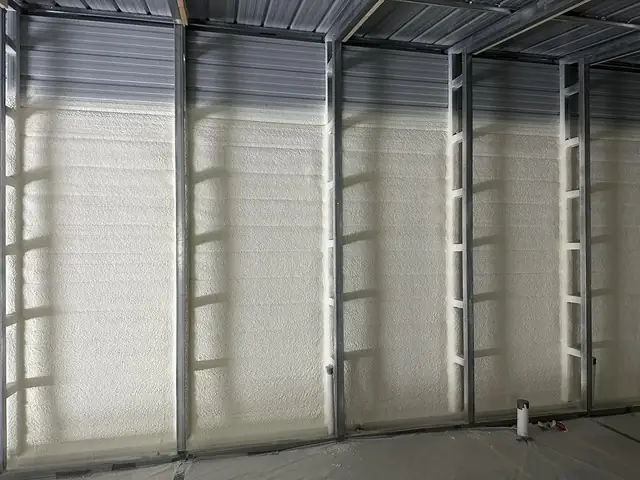 Spray foam applied between the steel columns of a metal building, covering the full height of the wall panels.