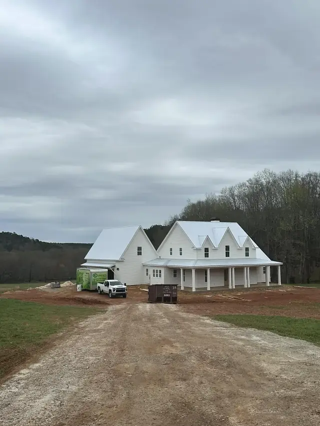 White farmhouse on a rural lot with the Green Earth truck and trailer parked alongside during a job.