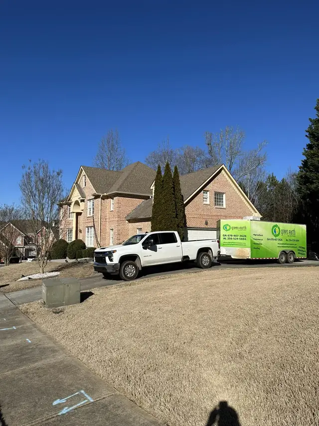 Green Earth truck and branded trailer on the driveway of a large brick home during an insulation job.