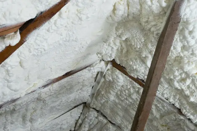 Close view of thick white spray foam covering an attic roof deck and the timber rafters.