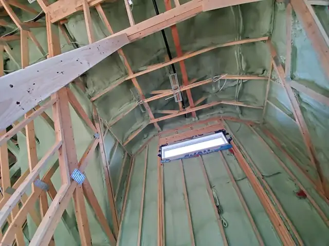 Roof deck of a new build coated in green spray foam, seen from inside the open framing.