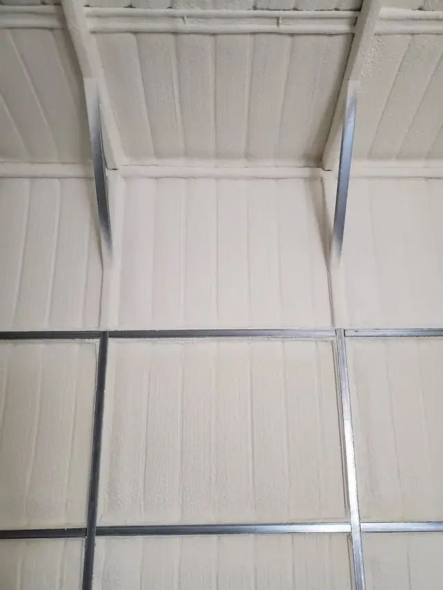 Metal building interior with pale spray foam covering the wall panels and roof deck between the steel framing.