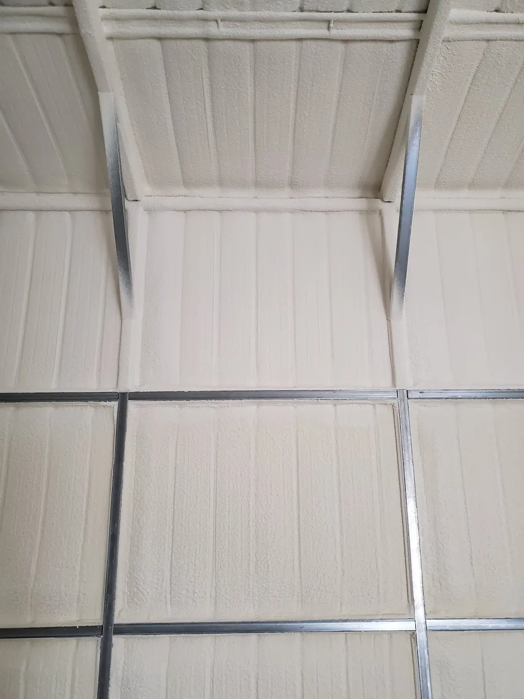 Metal building interior with pale spray foam covering the wall panels and roof deck between the steel framing.
