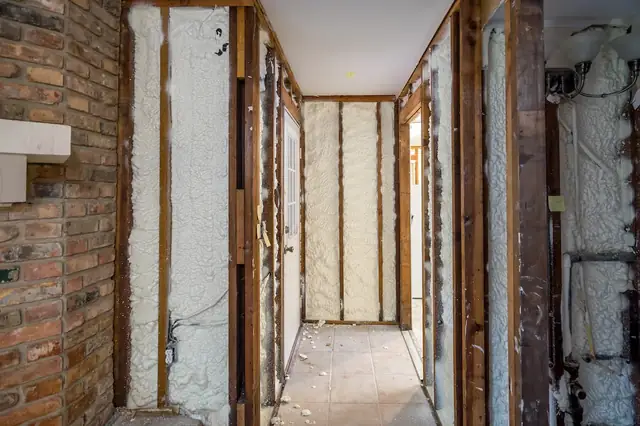 Narrow hallway under renovation with spray foam between the studs beside an exposed brick wall.