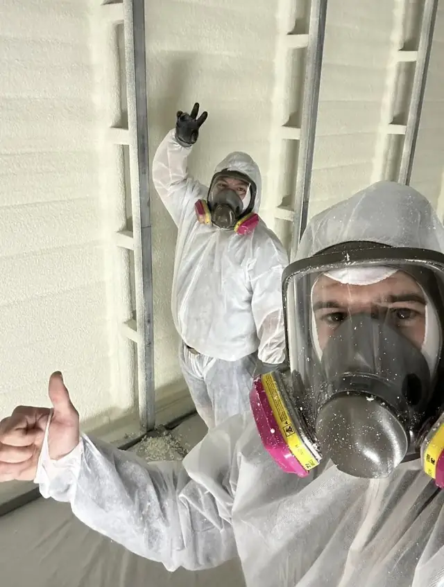 Two Green Earth technicians in protective suits and respirators inside a building with freshly sprayed walls.